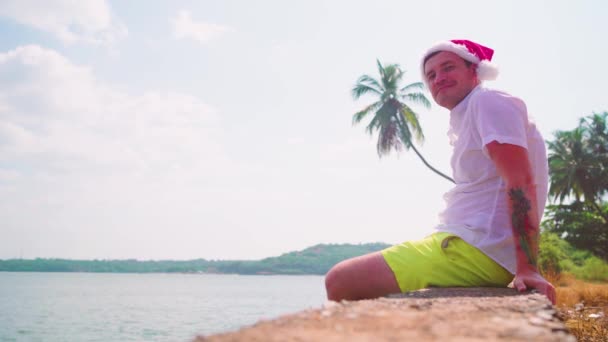 Mladý Muž Santa Klobouk Sedí Pláži — Stock video