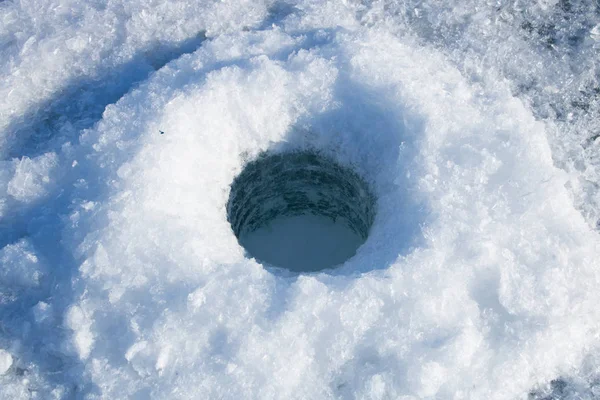 Drilled hole in the ice. Winter fishing on the river.