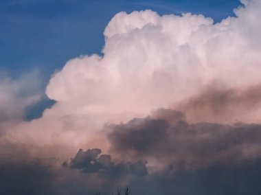 Gök gürültüsü bulutları, mavi gökyüzüne karşı pembe, güneş tarafından arkadan aydınlatılmış.