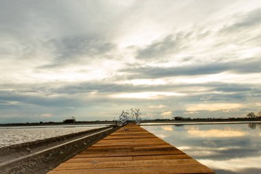Ahşap köprü ve su yüzeyinden günbatımı ışığı yansıtır.