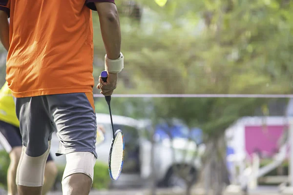 Elderly man Hand holding a badminton racket Background blur tree in park.