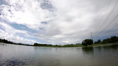 Yüksek gerilim güç direği nehir üzerinde eğilerek ve bulutlar gündüz parlak gökyüzünde hızlı hareket ediyor.