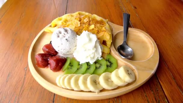 ワッフルに甘い水を注ぎ テーブルの上の木製のプレートにバナナ キウイ イチゴなどのアイスクリームとフルーツを注ぎます — ストック動画