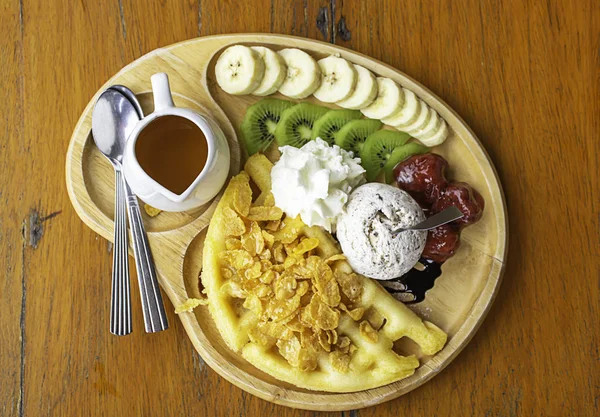 Sweet water pour on the waffle with ice cream and fruits including bananas, kiwi and strawberries in wooden plate on table.
