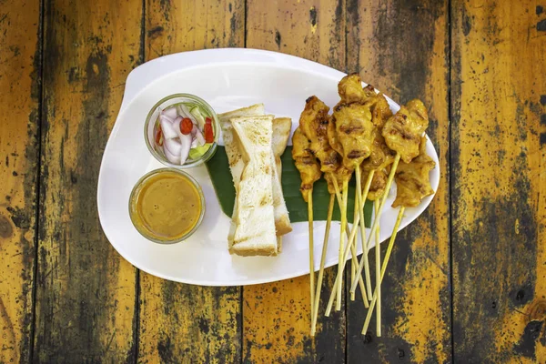 Satay de cerdo con leche de coco y pan con salsa en plato de plástico blanco sobre mesa de madera . — Foto de Stock