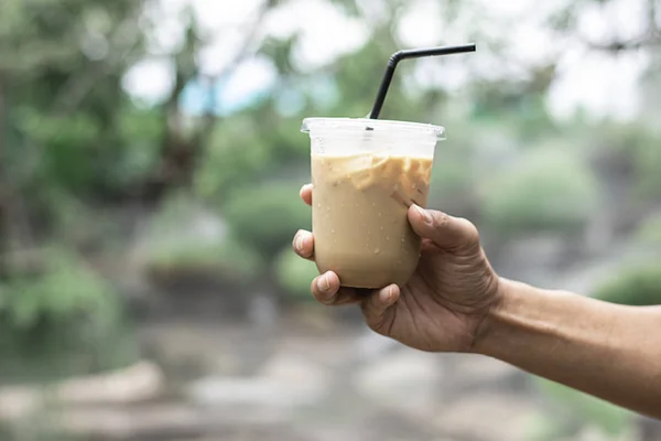 Mão segurando um copo de café expresso frio Fundo borrado vista árvore . — Fotografia de Stock