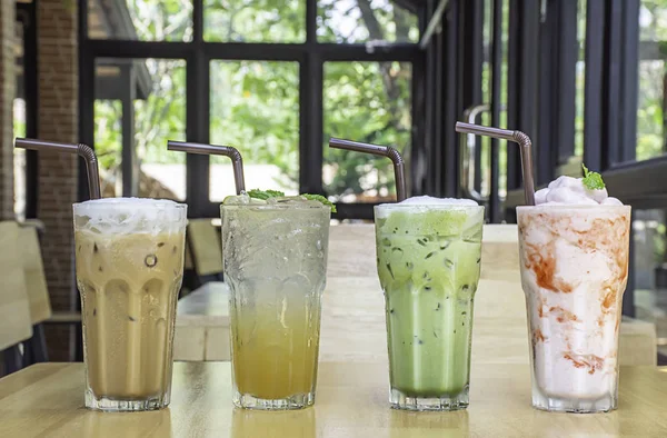 Iced Coffee, Honey Lemon Soda , iced green tea and strawberry smoothie in glass on the wooden table Background glass windows and  tree.