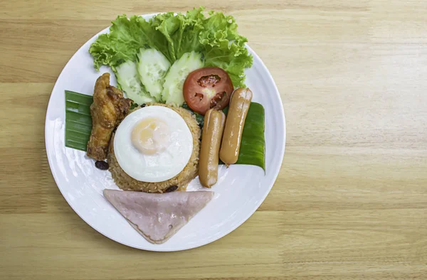 Американский жареный рис с колбасой, ветчиной, яйцами, курицей, помидорами, огурцом, на банановых листьях в белом блюде . — стоковое фото