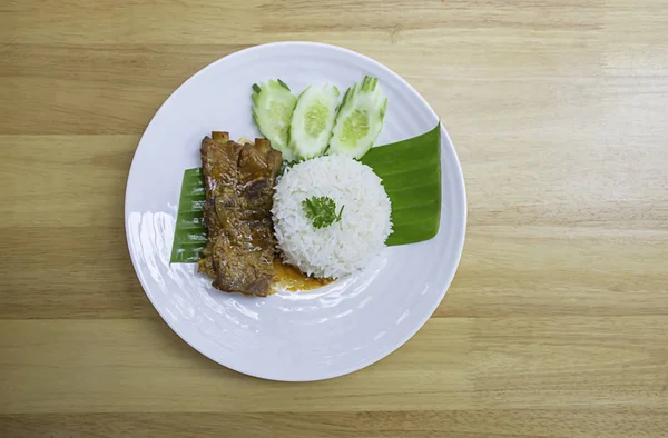 香蕉叶上的米饭和猪肉条木桌上的白盘上有黄瓜. — 图库照片