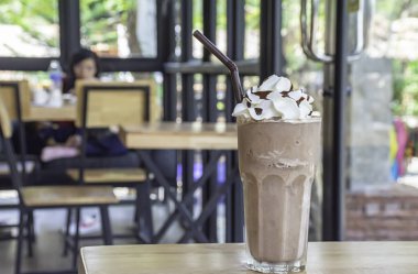 Soğuk kakao, cam tepesinde krem şanti, ahşap masa, cam pencereler ve ağaç..