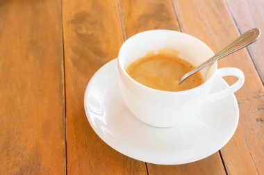 Tahta bir masanın üstünde çay tabağı olan beyaz bir fincanda sıcak kahve..