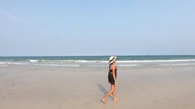 Asyalı kadınlar şapka takıyor ve siyah elbiseler yürüyor ve denizin dalgaları kumsala vuruyor..