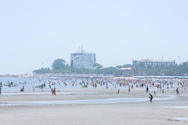 Birçok turist dalgaların çekildiği sahilde yürür. Arka plan denizi ve Tayland 'da Chonburi' deki Bangsaen Sahili 'ndeki büyük binalar. 21 Haziran 2020