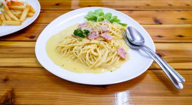 Spagetti, ahşap bir masada beyaz tabakta kızarmış peynir..