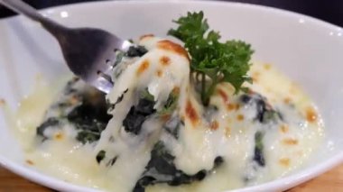 Peynirli fırınlanmış ıspanak beyaz tabakta çatal tarafından kepçelenir..