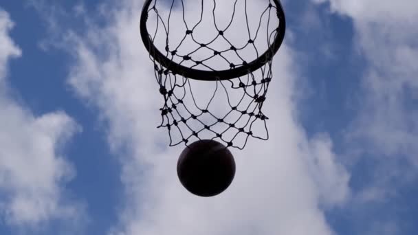 La vista inferior del clip lento de la pelota flotando en el aro de baloncesto y la red Fondo Hermosas nubes Cielo . — Vídeos de Stock