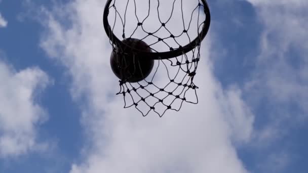 La vista inferior del clip lento de la pelota flotando en el aro de baloncesto y la red Fondo Hermosas nubes Cielo . — Vídeos de Stock
