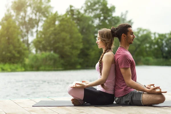 Woman and man practicing yoga in nature. Couple meditation. Copy space