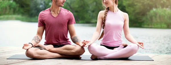 Couple practicing yoga in nature near the water. Couple meditation.