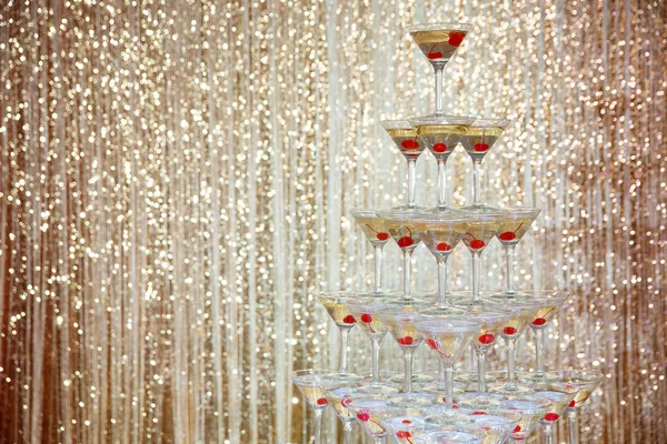 Sparkling champagne pyramid, tower of glasses at the party in front of golden wall