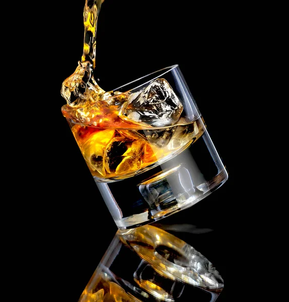 Nakloněná stylová sklenice whisky. Lití přes kostky ledu na černou — Stock fotografie