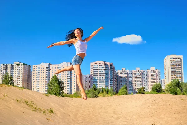 幸せな若い女性ジャンプオン砂浜背景に対して街並みで晴れた夏の日 — ストック写真