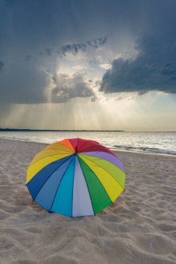 Dramatik fırtınalı bulutlara karşı sahilde çok renkli şemsiye