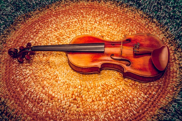 An old violin on a colored knitted rug of warm tones