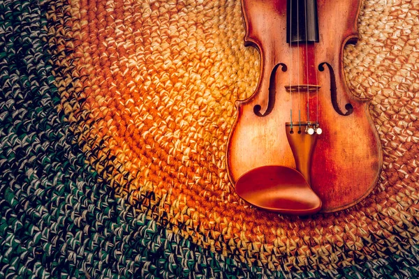 An old violin on a colored knitted rug of warm tones