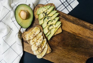 Tost avokado, susam ve bütün tahıl ekmeği fıstık ezmesi ve muzlu ekmek ve keten tohumu kepekli ekmek üzerinde. Sağlıklı kahvaltı. Üstten görünüm