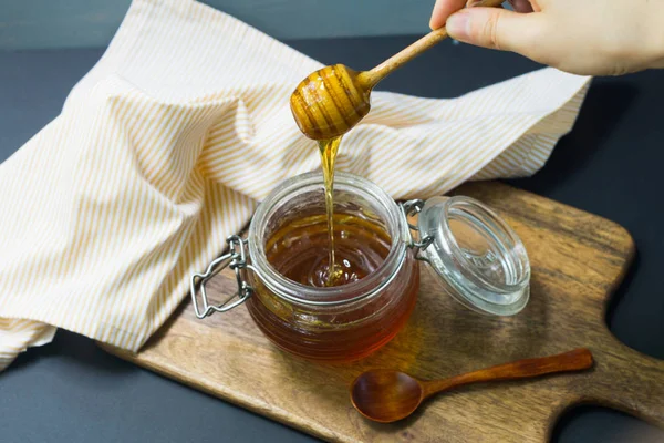 Honung i en burk och hand med en trä honung skopa på en träskiva med en linneduk — Stockfoto