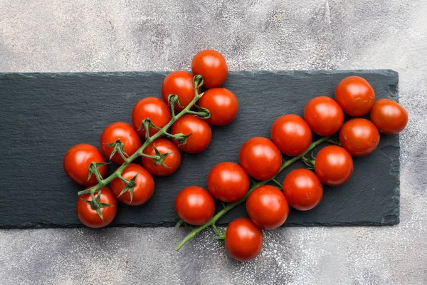 Świeże pomidory cherry na oddział na czarnym tle betonowych. — Zdjęcie stockowe
