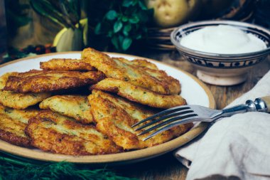 Tavada patates gözlemesi (rosti, kartoffelpuffer, draniki, kıymalı patates Latkeler): geleneksel patates börek sourcream ve yeşillik bir ahşap zemin üzerine
