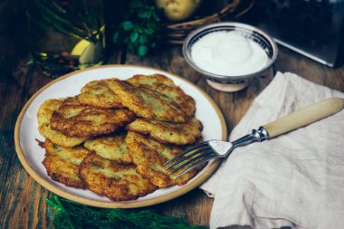 Tavada patates gözlemesi (rosti, kartoffelpuffer, draniki, kıymalı patates Latkeler): geleneksel patates börek sourcream ve yeşillik bir ahşap zemin üzerine