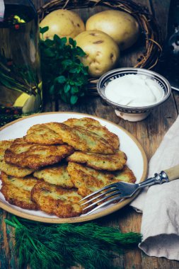 Tavada patates gözlemesi (rosti, kartoffelpuffer, draniki, kıymalı patates Latkeler): geleneksel patates börek sourcream ve yeşillik bir ahşap zemin üzerine