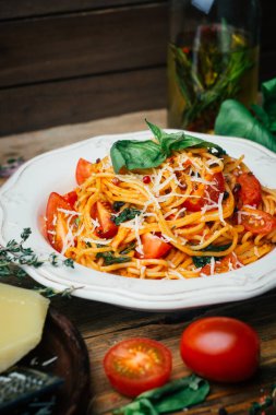 Spagetti makarna domates sos, parmesan ve fesleğen beyaz tabakta. Klasik domates spagetti: Vejetaryen domates fesleğen makarna. Eski ahşap arka plan