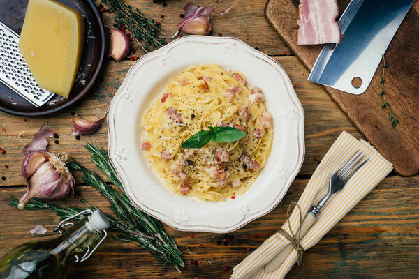 Спагетти Карбонара. Паста алла карбонара со сливочным соусом, беконом и перцем на белой тарелке. Старый деревянный фон
