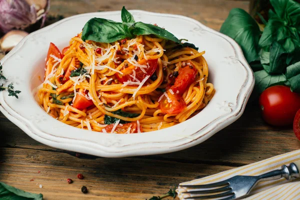 Spaghetti pasta with tomato sauce, parmesan and basil on a white plate. The classic tomato spaghetti: vegetarian tomato basil pasta. Old wooden background