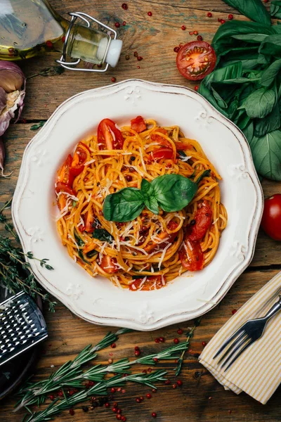 Spaghetti pasta with tomato sauce, parmesan and basil on a white plate. The classic tomato spaghetti: vegetarian tomato basil pasta. Old wooden background
