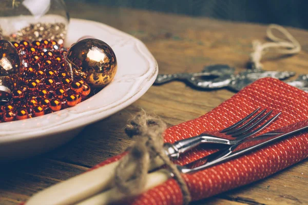 Holiday Christmas food background concept. Christmas table with a white plate and Christmas decorations. Set of cutlery knife and fork on a red napkin. Old rustic vintage wood background. Copy space.