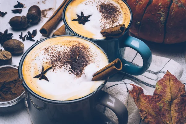 Pumpkin spice latte or coffee with cinnamon and nutmeg. Autumn, fall or winter hot drink. Old white wooden background with yellow leaves and pumpkins