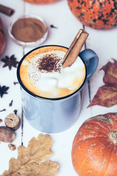 Pumpkin spice latte or coffee with cinnamon and nutmeg. Autumn, fall or winter hot drink. Old white wooden background with yellow leaves and pumpkins