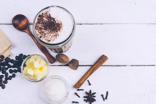 Bulletproof coffee. Ketogenic diet coffee with coconut oil and butter (ghee). Cup of bulletproof coffee and ingredients, paleo diet. On white wooden background