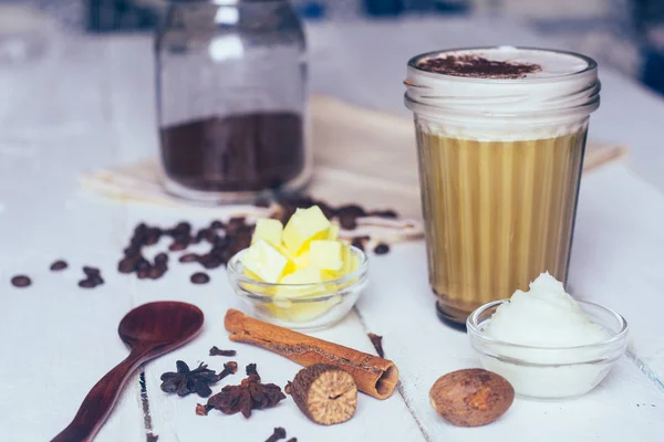 Bulletproof coffee. Ketogenic diet coffee with coconut oil and butter (ghee). Cup of bulletproof coffee and ingredients, paleo diet. On white wooden background