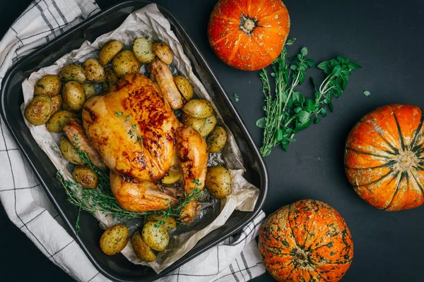 Roasted chicken with thyme served on black baking dish with potatoes, oranges and spices on wooden table. Thanksgiving or Christmas dinner. Top view