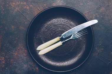 Boş kahverengi plaka (seramik) üzerinde bıçak ve çatal ile karanlık bir arka plan. Kopya alanı.