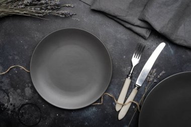 Boş gri plaka (seramik) üzerine koyu gri bir arka plan ile bıçak ve çatal, lavanta ve peçete bir buket ile dekore edilmiştir. Gri minimalist kavramı. Kopya alanı.