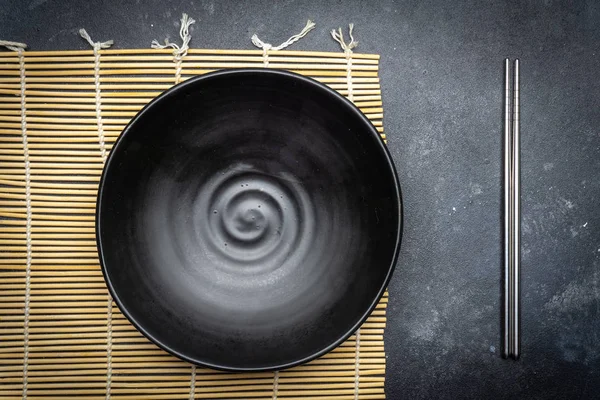 Empty plate (dark) and Chinese chopsticks on a dark background. Asian style, Asian cuisine. Copy space.