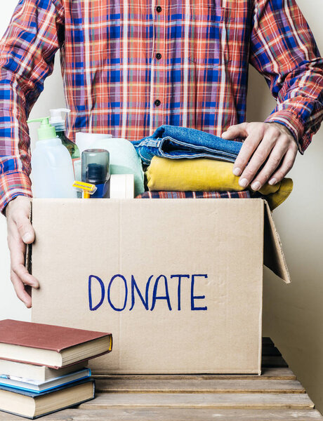 CLOTHES DONATION AND FOOD DONATION CONCEPT. A man holding a donation box with clothes, shoes and hygiene products.