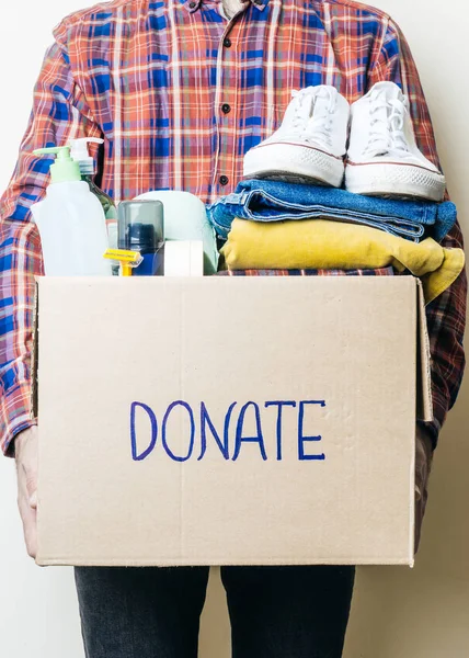 CLOTHES DONATION AND FOOD DONATION CONCEPT. A man holding a donation box with clothes, shoes and hygiene products.